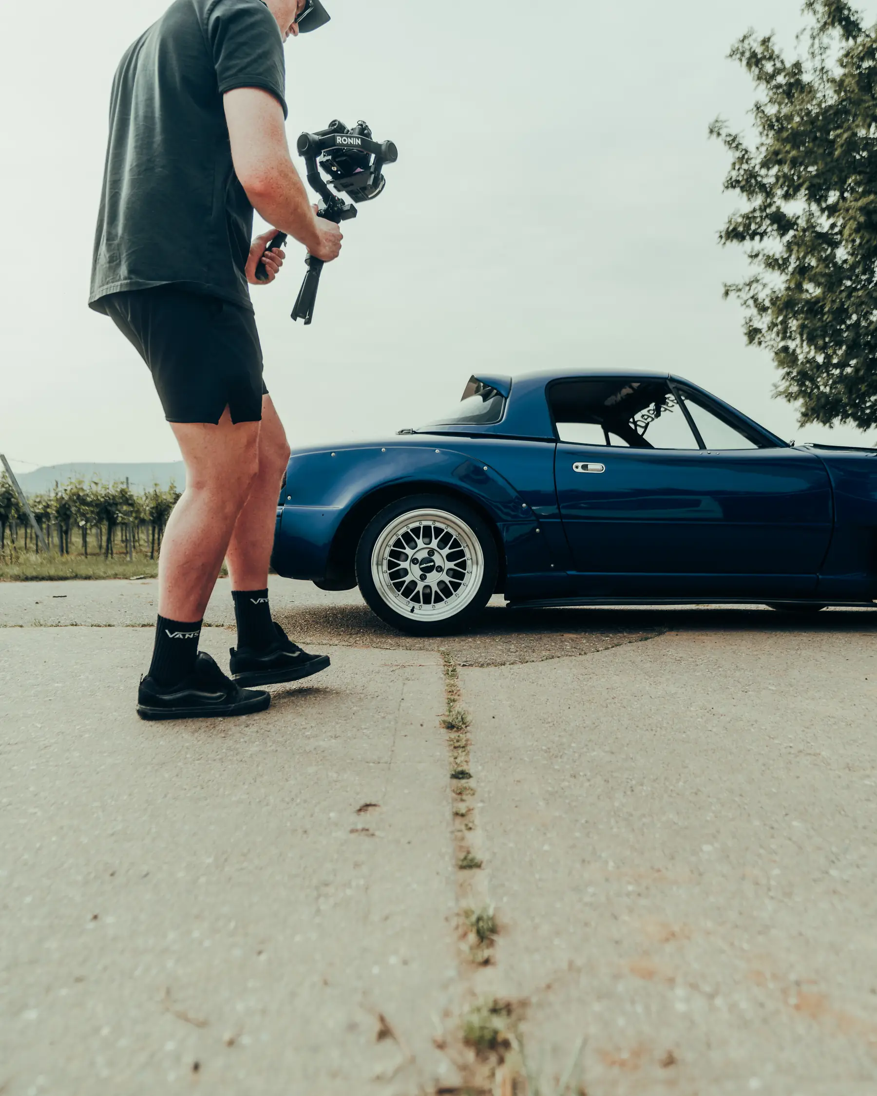 Seitenansicht eines dunkelblauen Mazda MX-5, davor Bastian Obitz mit Gimbal, angeschnitten