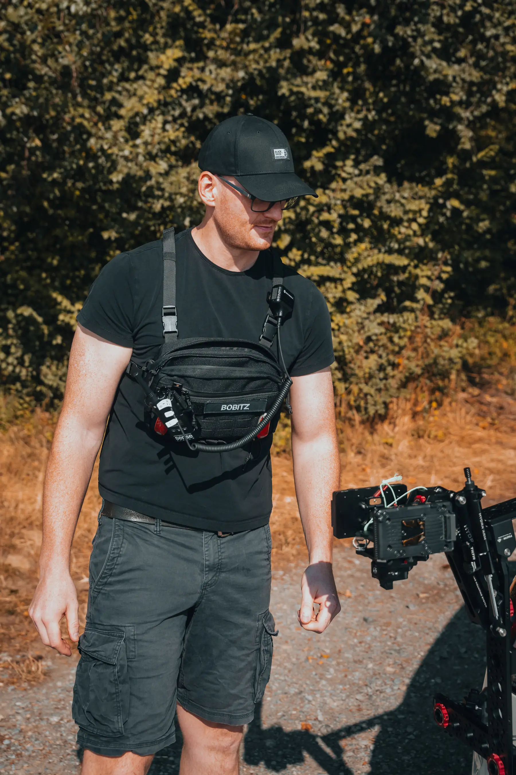 Bastian Obitz mit Brusttasche geht auf ein aufgebautes Kamera-Rig an einem Motorrad zu